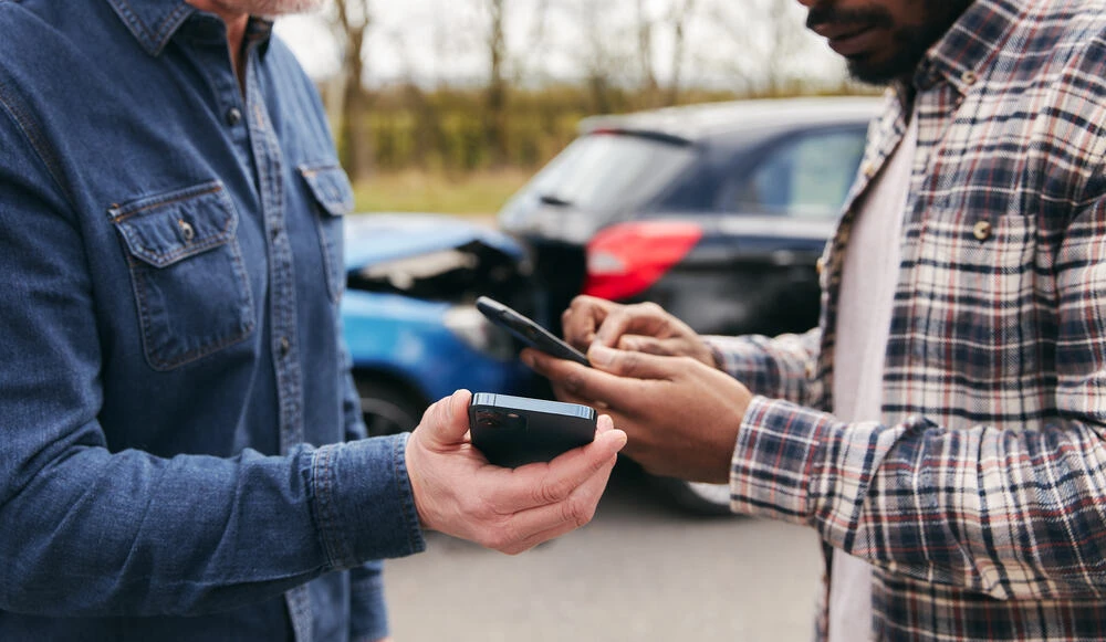 Younger and older drivers at side of the road exchanging car insurance details after traffic accident using mobile phones