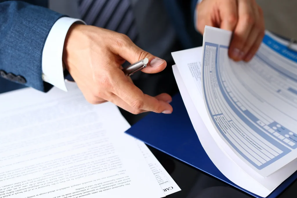 Male arm in suit offer insurance form clipped to pad and silver pen to sign closeup